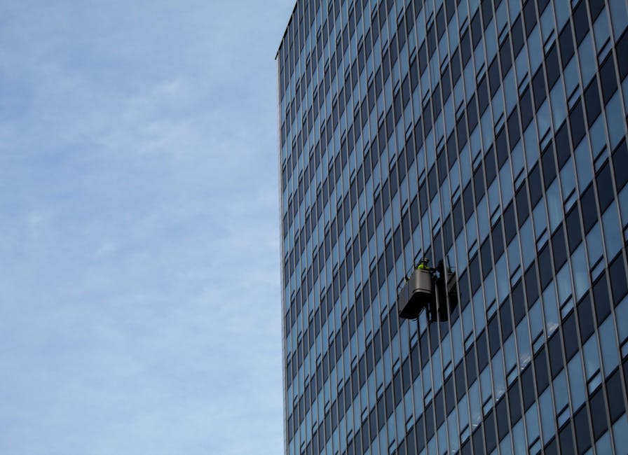 Window cleaners working on a skyscraper's glass facade against a clear sky.